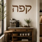 מדבקה עם אותיות עבריות שחורות על קיר בסלון עם ספה אפורה ושטיח בהיר