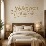 מדבקה עם קליגרפיה עברית ולב קטן על קיר בחדר ילדים עם שולחן קטן וכיסא עץ.