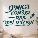 מדבקת טקסט בעברית עם כוכב נופל על קיר בחדר ילדים עם צעצועים בצבעים בהירים ושולחן קטן.