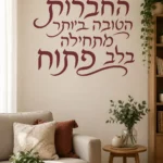 מדבקת קליגרפיה עברית על קיר בסלון עם כורסאות צבעוניות ותאורה חמימה.