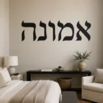 מדבקת אותיות עבריות שחורות על קיר לבן בחדר עם ספה צבעונית ושולחן עץ.