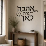 מדבקת קליגרפיה עברית עם לב קטן על קיר בחדר ילדים עם מנורה וצעצועים ברקע.