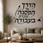 מדבקת קליגרפיה עברית על קיר בסלון עם ספה אפורה ושולחן עץ כהה, תאורה רכה ברקע.