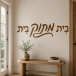 מדבקה עם קליגרפיה עברית שחורה על קיר בסלון עם ספה אפורה ושולחן קפה מעץ כהה.