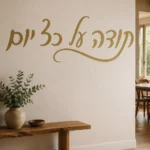 מדבקת קליגרפיה עברית על קיר בסלון עם ספה אפורה ושולחן עץ קטן