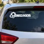 מדבקה עם הכיתוב 'מכונאי בנשמה' על השמשה האחורית של רכב כחול ברחוב שקט.