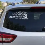 מדבקה שחורה עם עיצוב עץ על השמשה האחורית של רכב כחול ברחוב עירוני.