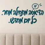 מדבקת טקסט עברי עם סמל לב על קיר בחדר ילדים עם צעצועים רכים ורקע בהיר