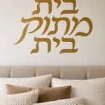 מדבקת קליגרפיה עברית על קיר בסלון עם ספה נוחה ותאורה רכה.
