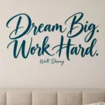 מדבקת 'Dream Big. Work Hard.' על קיר בחדר ילדים עם מדף ספרים וכריות צבעוניות.