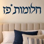 מדבקת טקסט עברי שחור עם כוכב קטן מעל על קיר בחדר ילדים עם צעצועים וצבעים נעימים.