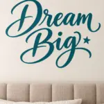 המדבקה 'Dream Big' על קיר בחדר ילדים עם מיטה לבנה וצעצועים צבעוניים סביב.